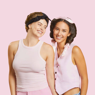 in Studiofoto vor dem hellrosa Hintergrund, der auch in image_0.png zu sehen ist, zeigt zwei junge Frauen in einer engen, freundschaftlichen Pose.